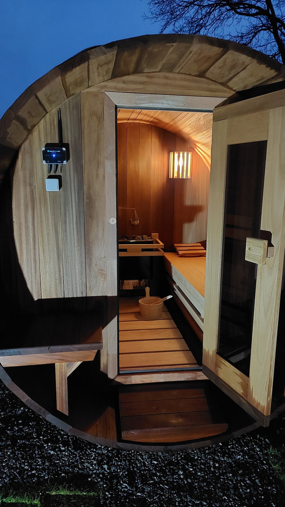 Sauna barrel extérieur du Gîte de Lierneux ouvert au crépuscule avec lumière chaude intérieure