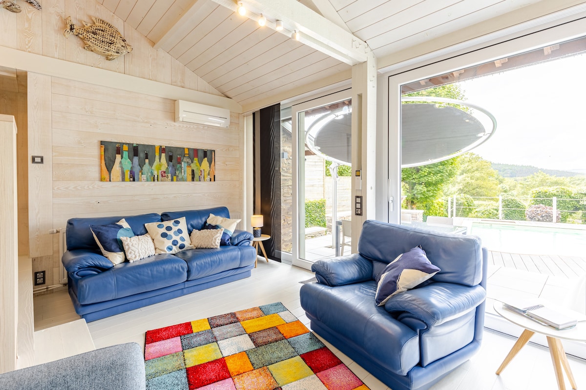 Salon lumineux du Gîte de Lierneux avec canapés en cuir bleu et vue panoramique sur la terrasse